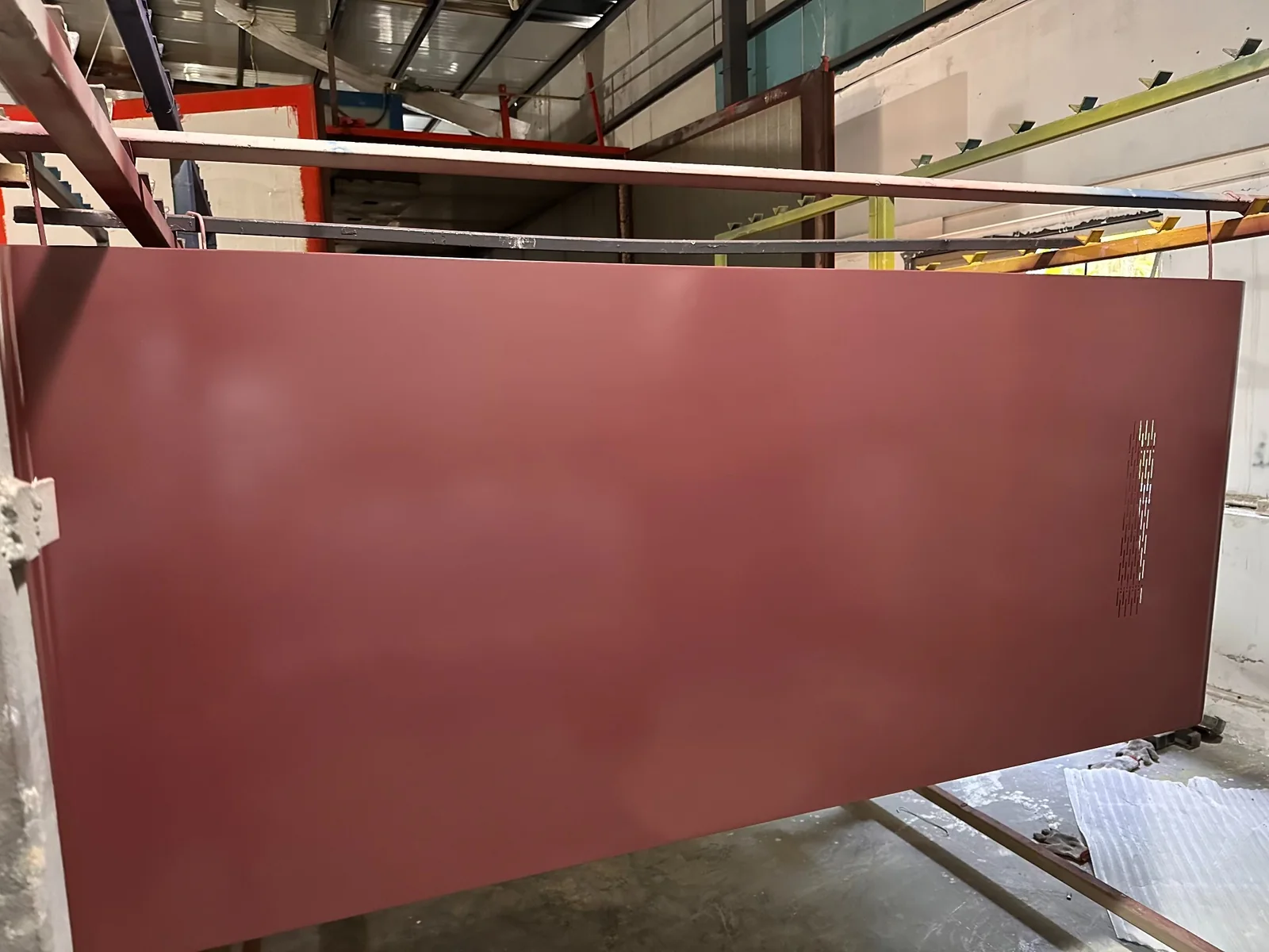 Burgundy-colored office pod panel face with ventilation slots on a factory rack