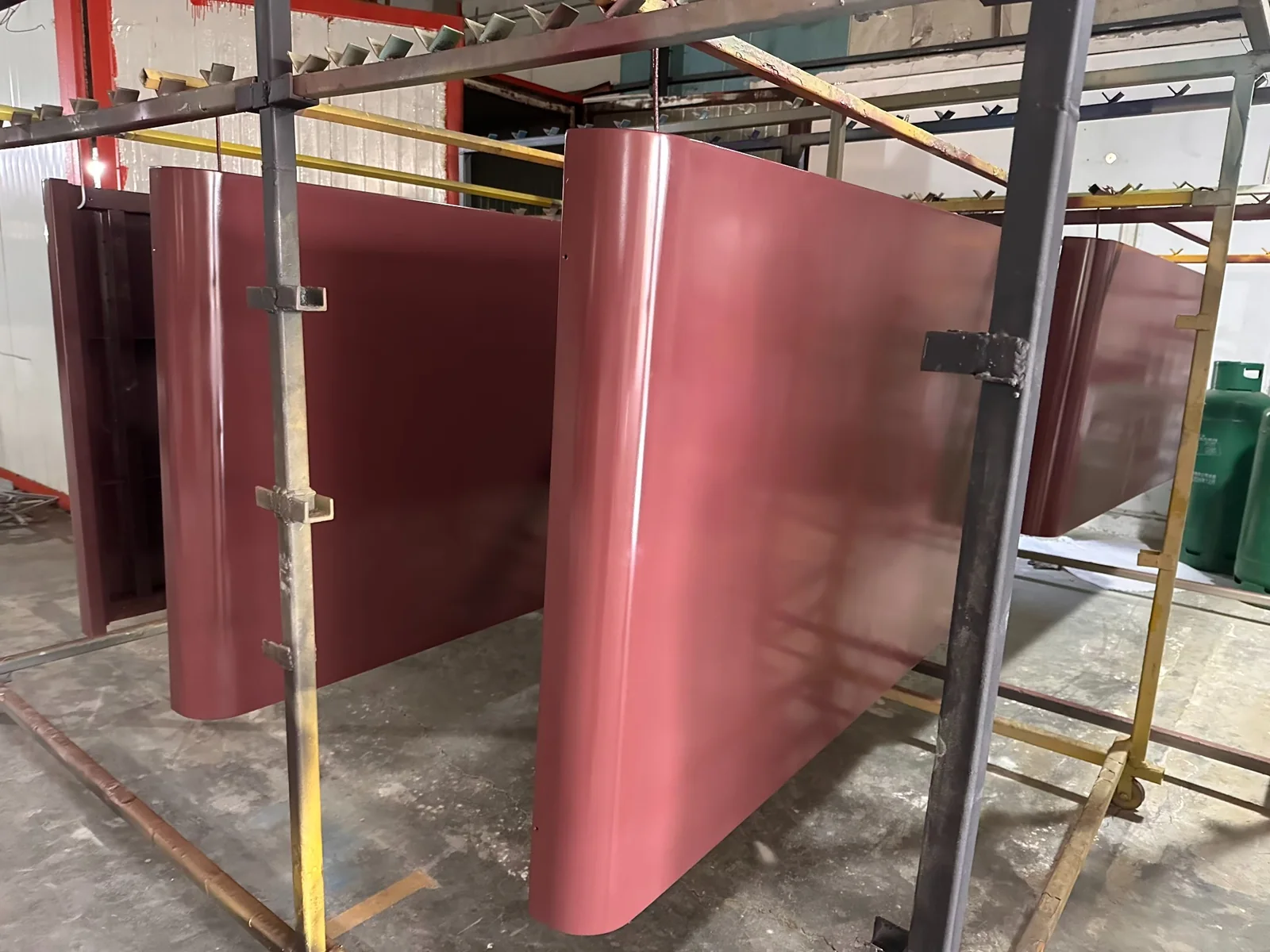 Multiple burgundy-colored curved office pod panels supported on factory racks