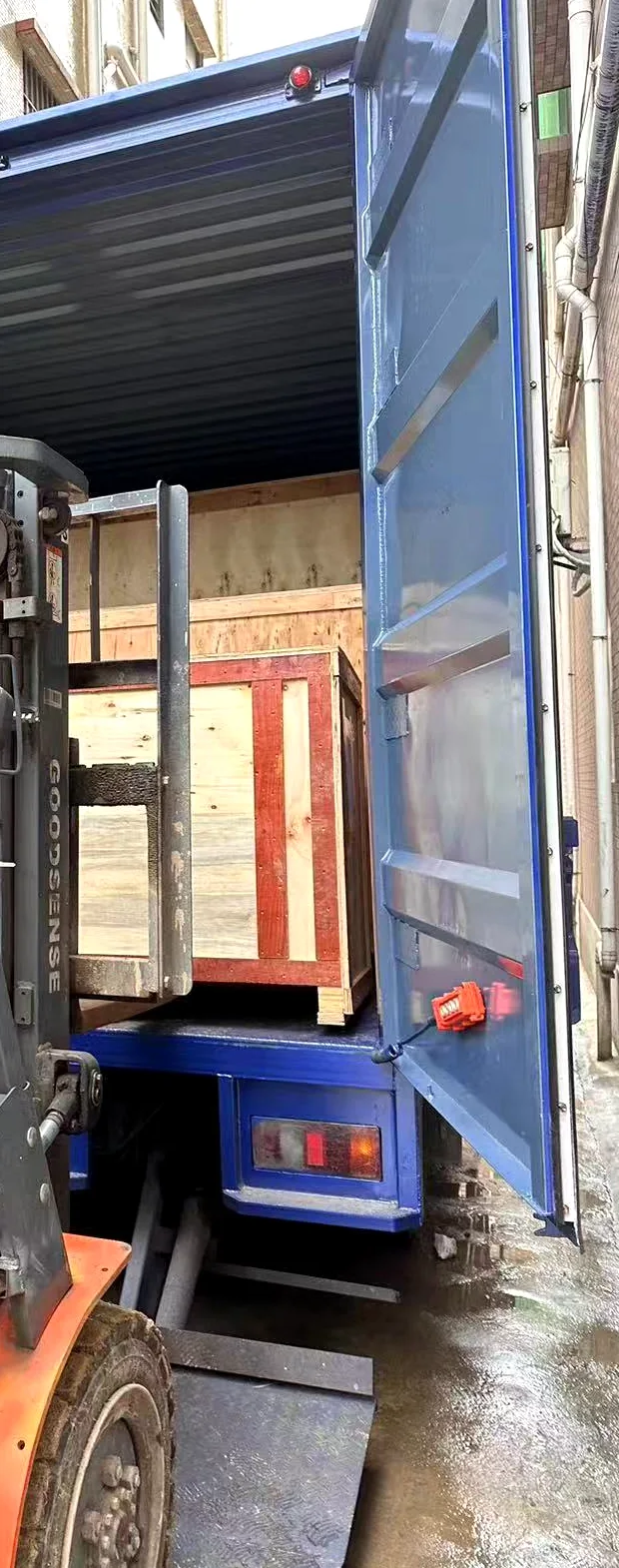 Forklift moving a closed wooden office pod crate into a cargo vehicle during factory loading