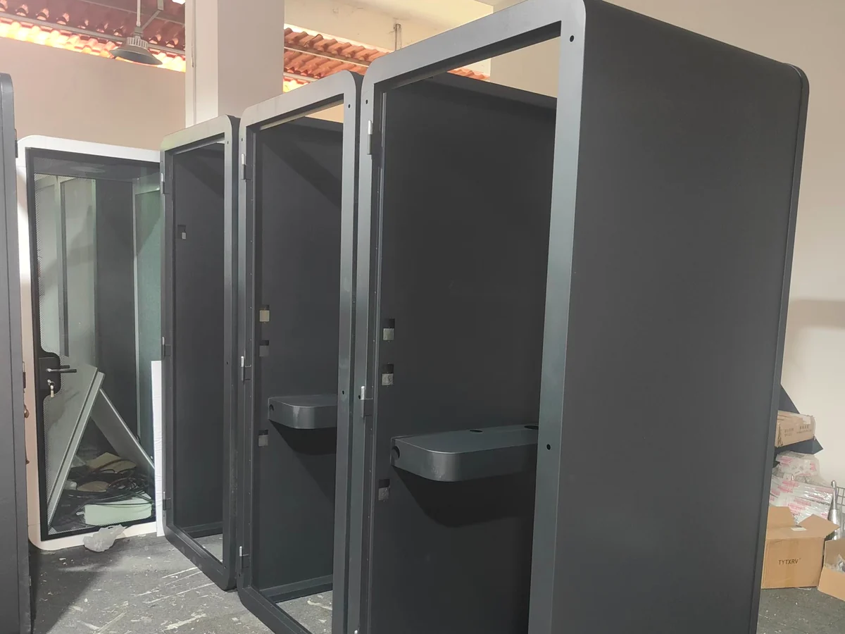 Dark office pod shells with open front frames and installed work surfaces in a factory assembly area