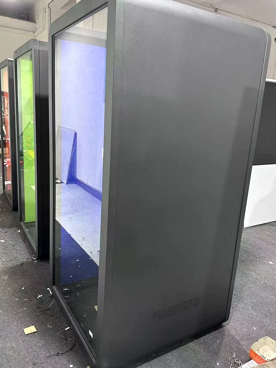 Dark office pod shell beside a front glazing frame with a lower perforated opening visible